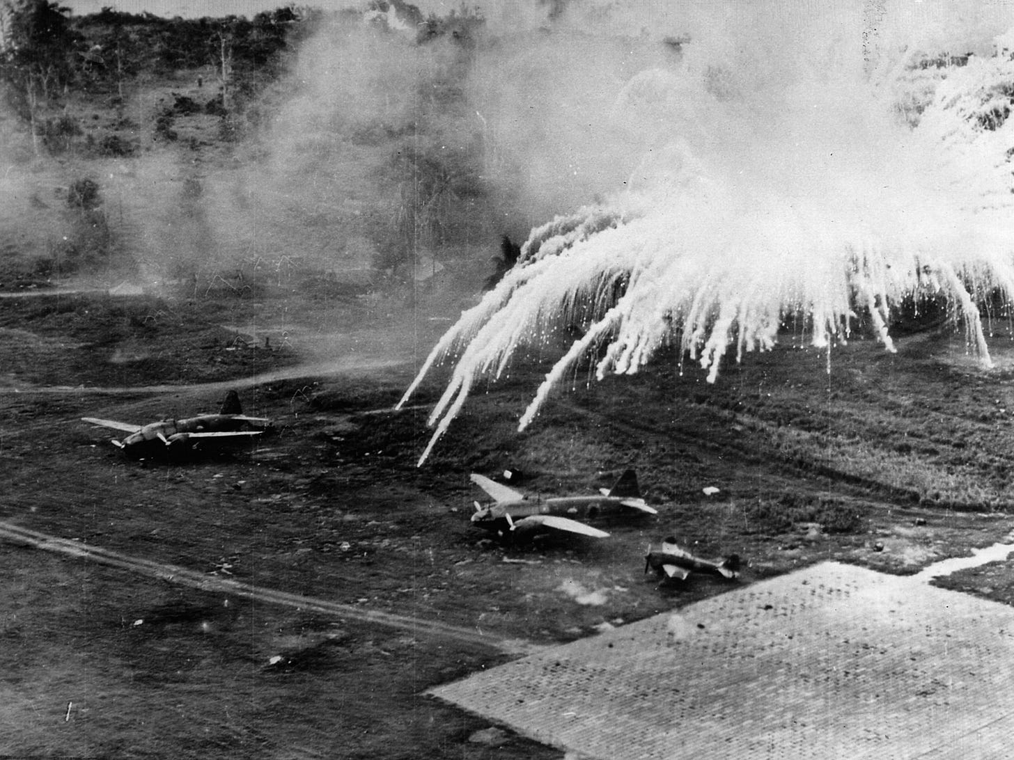 Explosions rock a Japanese airfield near Rabaul. U.S. B-25s and P-38s of the 5th Air Force hammered the site in an effort to put the airfield out of commission. Explosions rock a Japanese airfield near Rabaul. U.S. B-25s and P-38s of the 5th Air Force hammered the site in an effort to put the airfield out of commission.